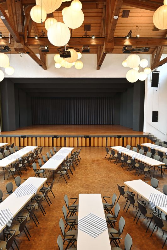 Moderner Saal Kurhaus Bad Hindelang mit festlich gedeckten Tischen, Holzbalkendecke und runden Papierlampions.