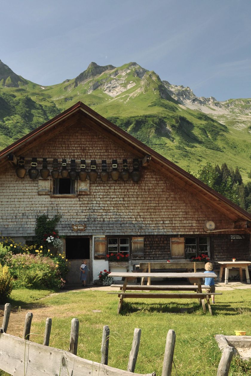 Die Hütte der Alpe Plättele im Obertal, im Vordergrund ist ein Holzzaun, im Hintergrund sind die Berge zu sehen.