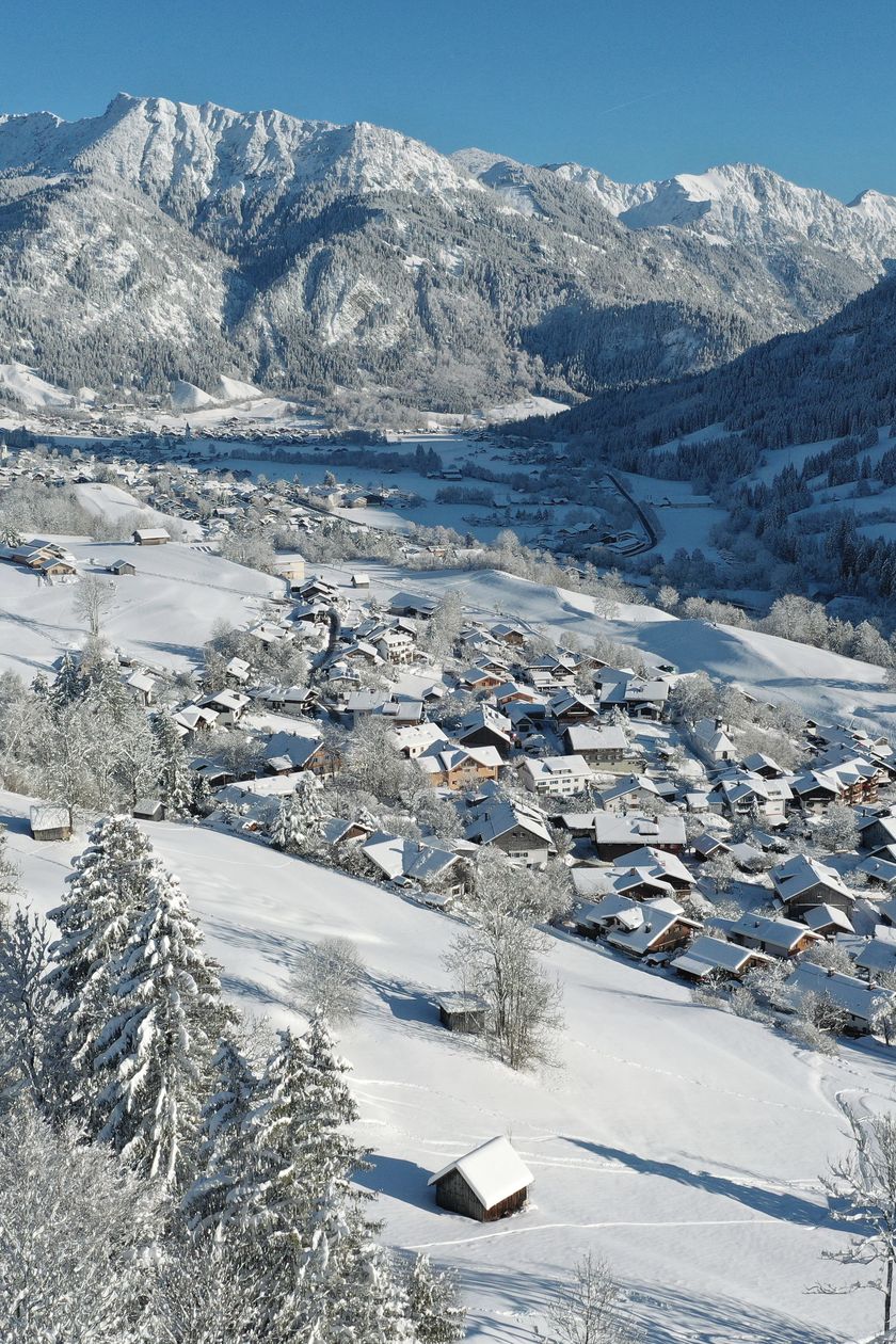 Winterlandschaft in Vorderhindelang mit verschneiten Bergen und verschneiten Häusern.