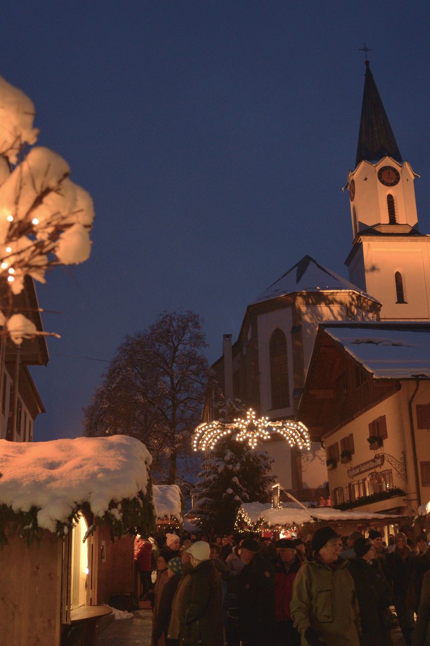 Eine weihnachtlich beleuchtete Straße auf der Menschen laufen, im Hintergrund eine beleuchtete Kirche.
